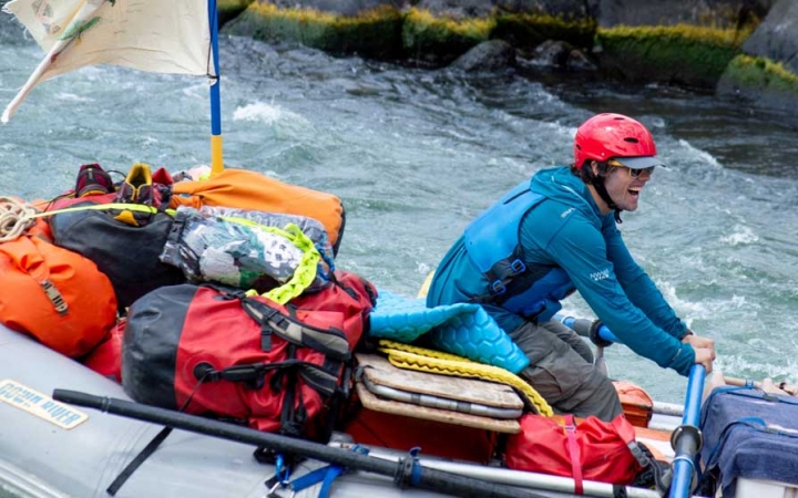 a person smiles as they captain a raft through whitewater 